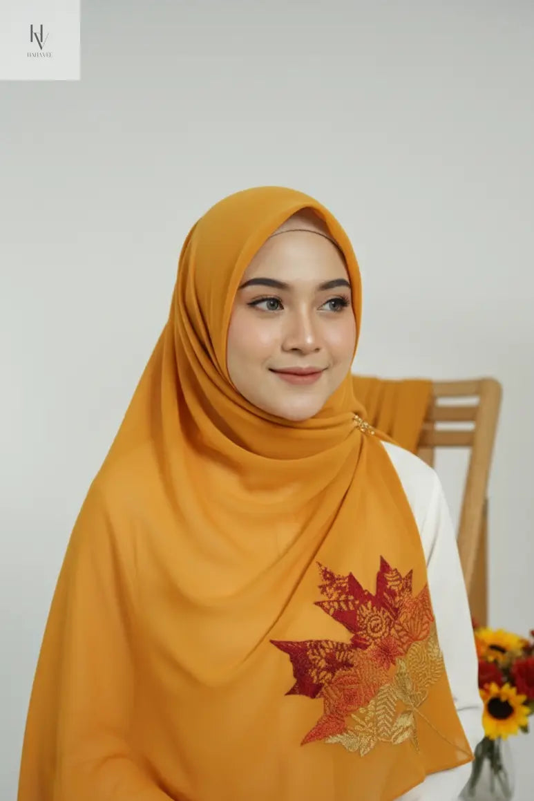 Woman wearing a mustard yellow hijab with floral patterns, sitting indoors.