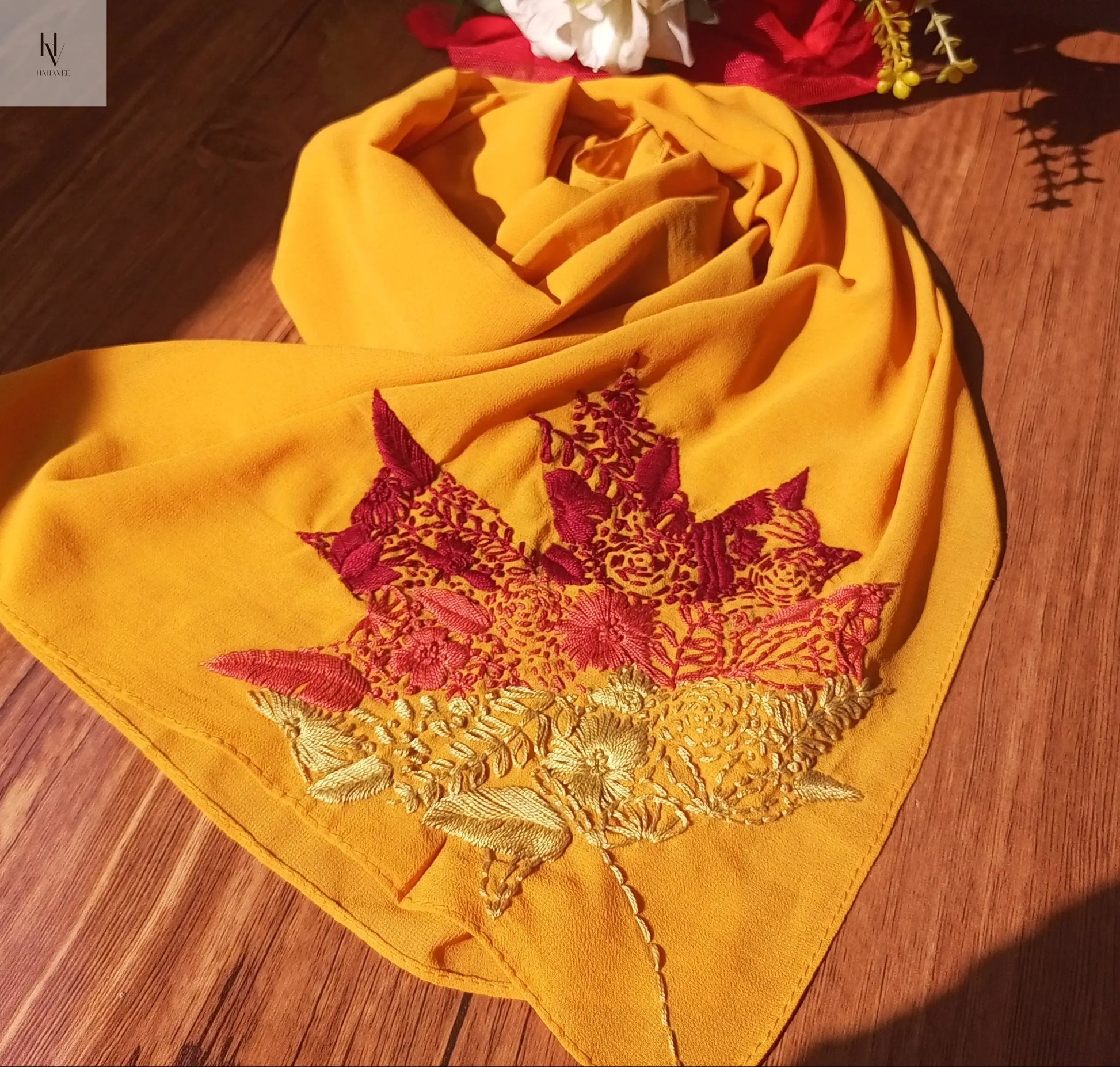 Yellow scarf with floral embroidery on a wooden surface with flowers in the background